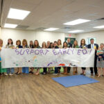 group of people holding handmade sign saying "support early ed"