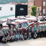 group of people stand in front of fleet of work vehicles